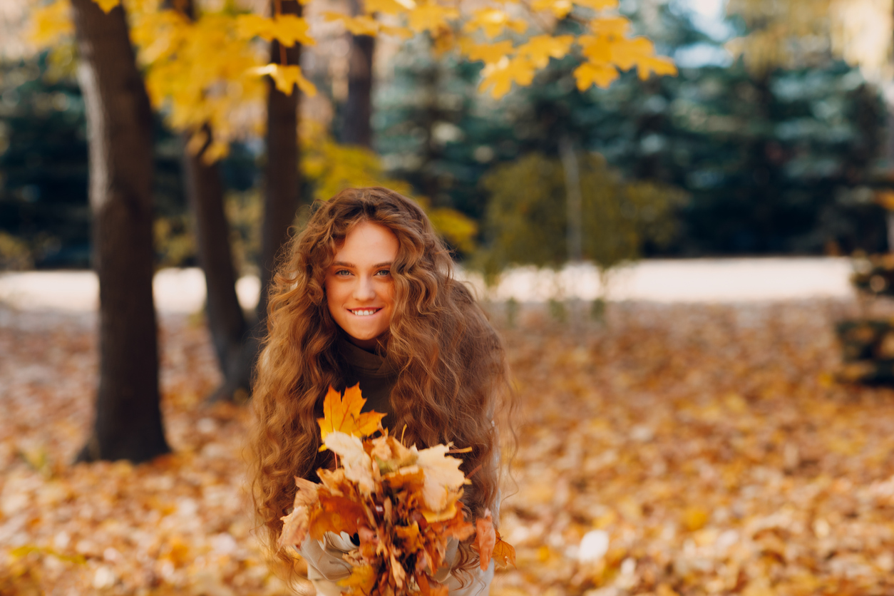 Smiling young woman enjoys the autumn weather in the forest with the yellow leaves at sunset